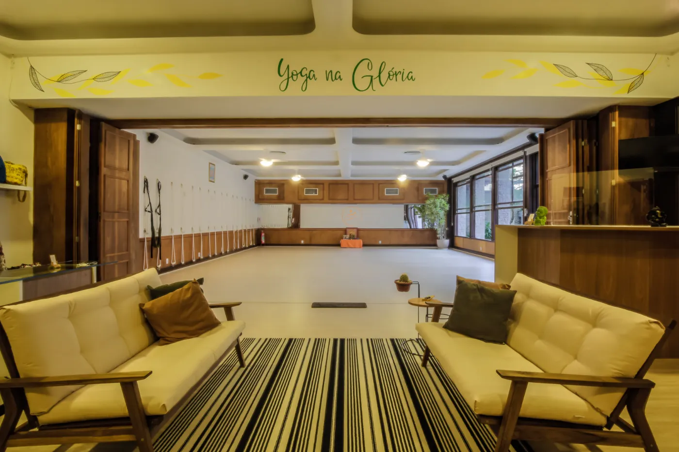 Lounge de espera do estúdio com bancos de madeira e a assinatura Yoga na Glória na parede